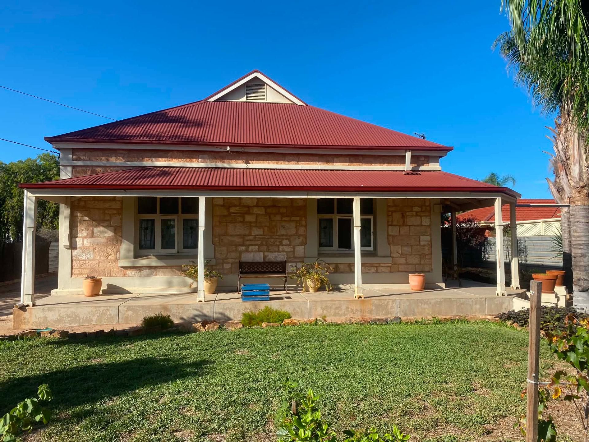 Heritage sandstone home with a red roof and newly replaced guttering along the verandah and eaves