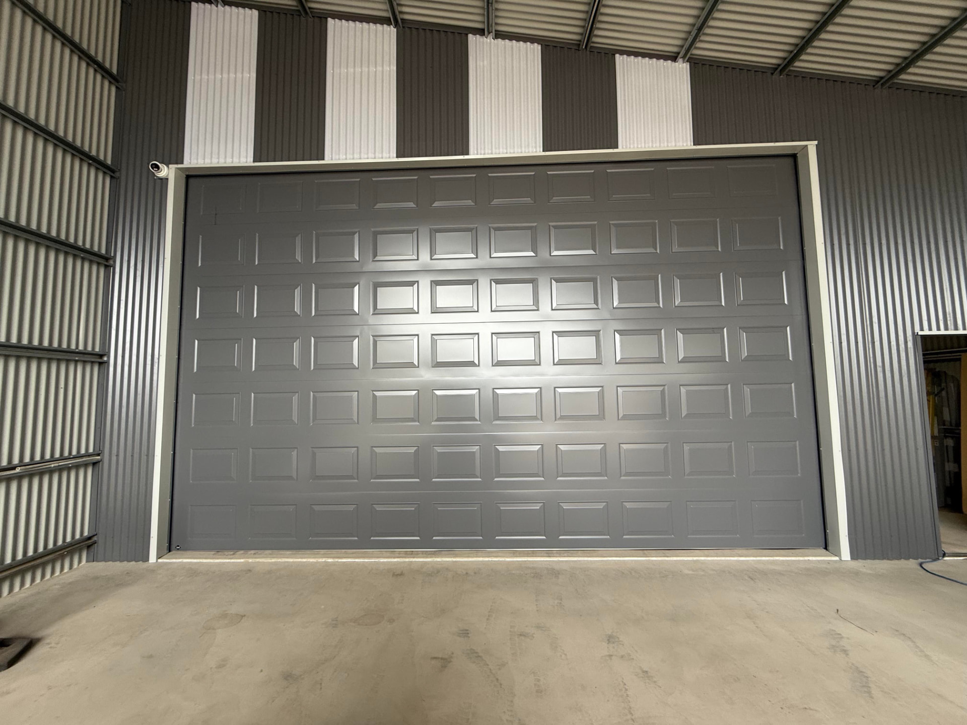 Front face of a full size B&D PFI Panel Lift Icon door in Basalt with the Statesman pressing, closed inside a large shed