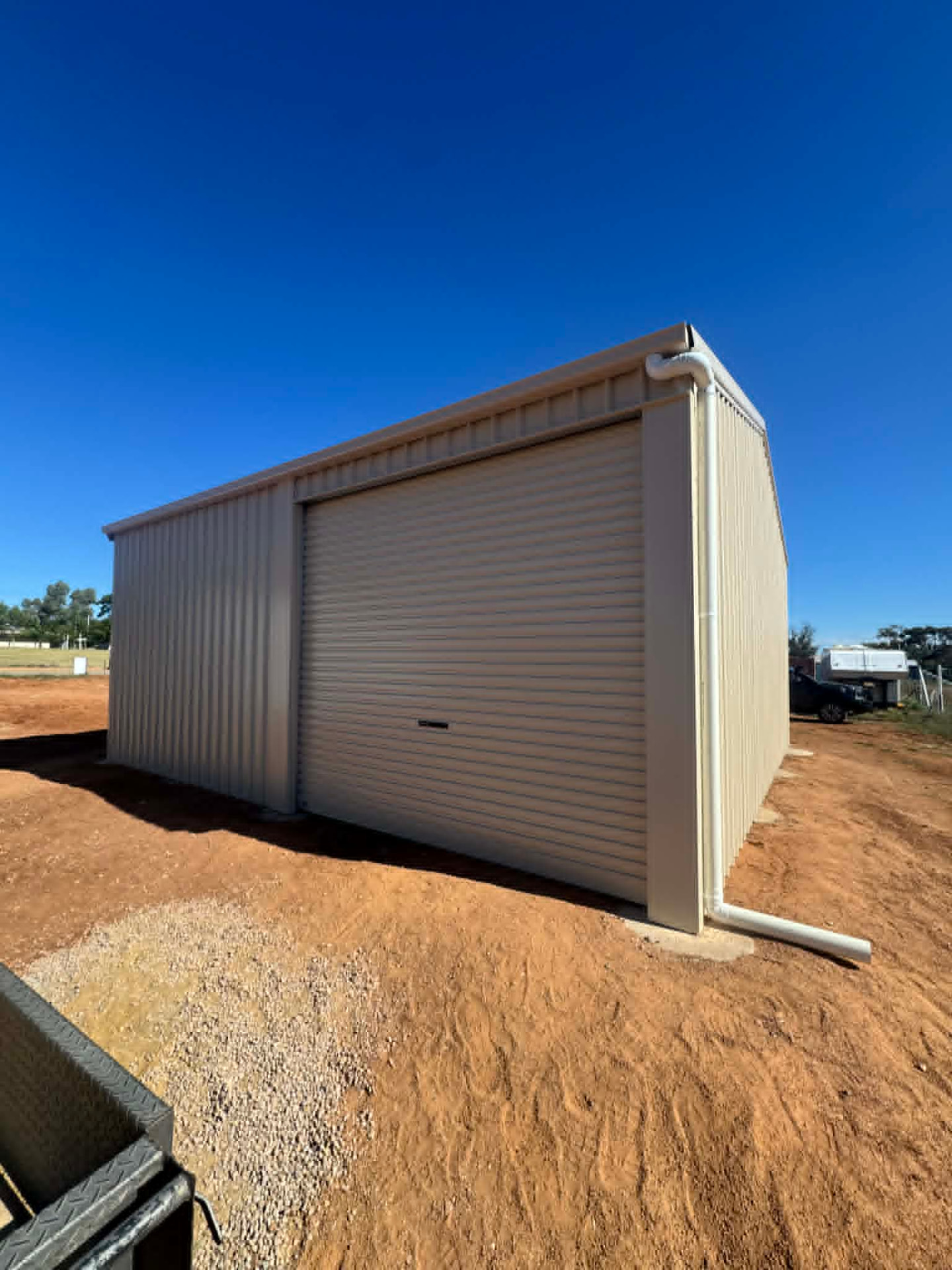 Completed steel shed with a cream roller door and downpipe on a prepared pad