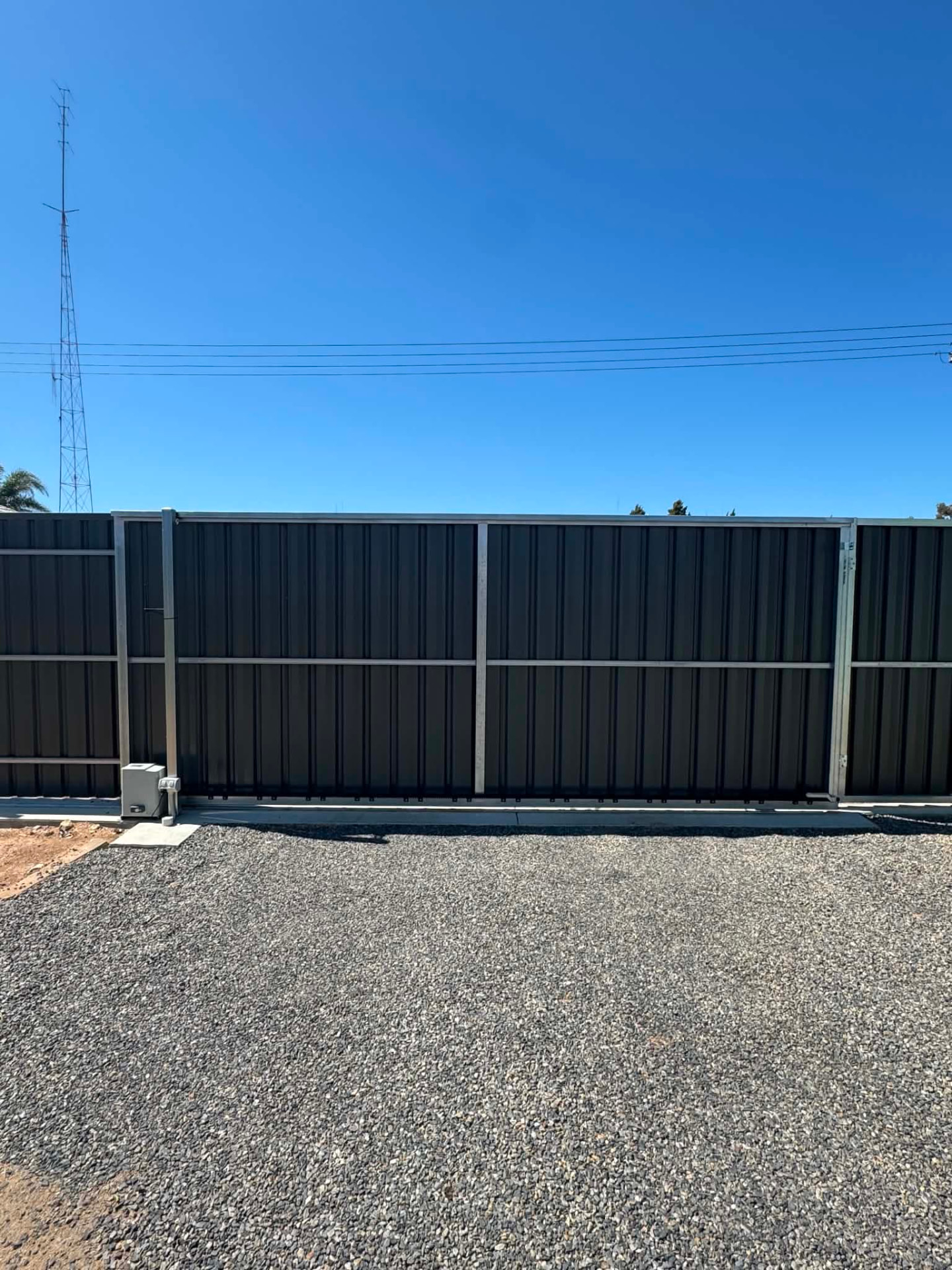 Dark automatic sliding gate closed across a gravel driveway with an ATA gate motor mounted at the base
