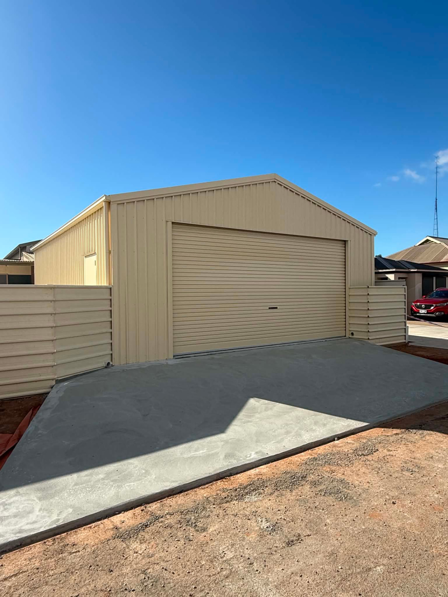 Completed cream gable steel shed with a roller door and matching colorbond fence panels