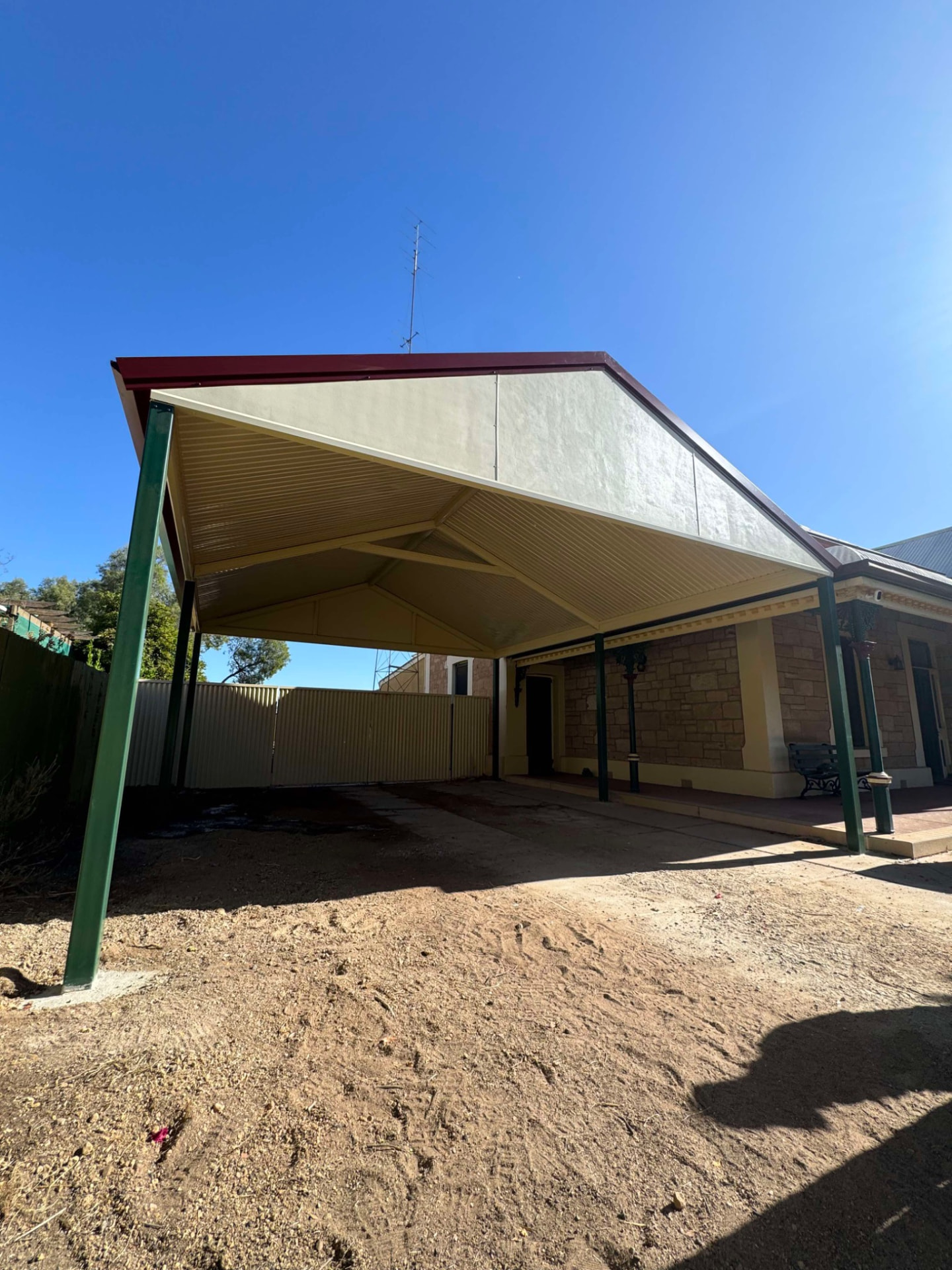 Completed gable-roof carport with green posts attached to a stone home