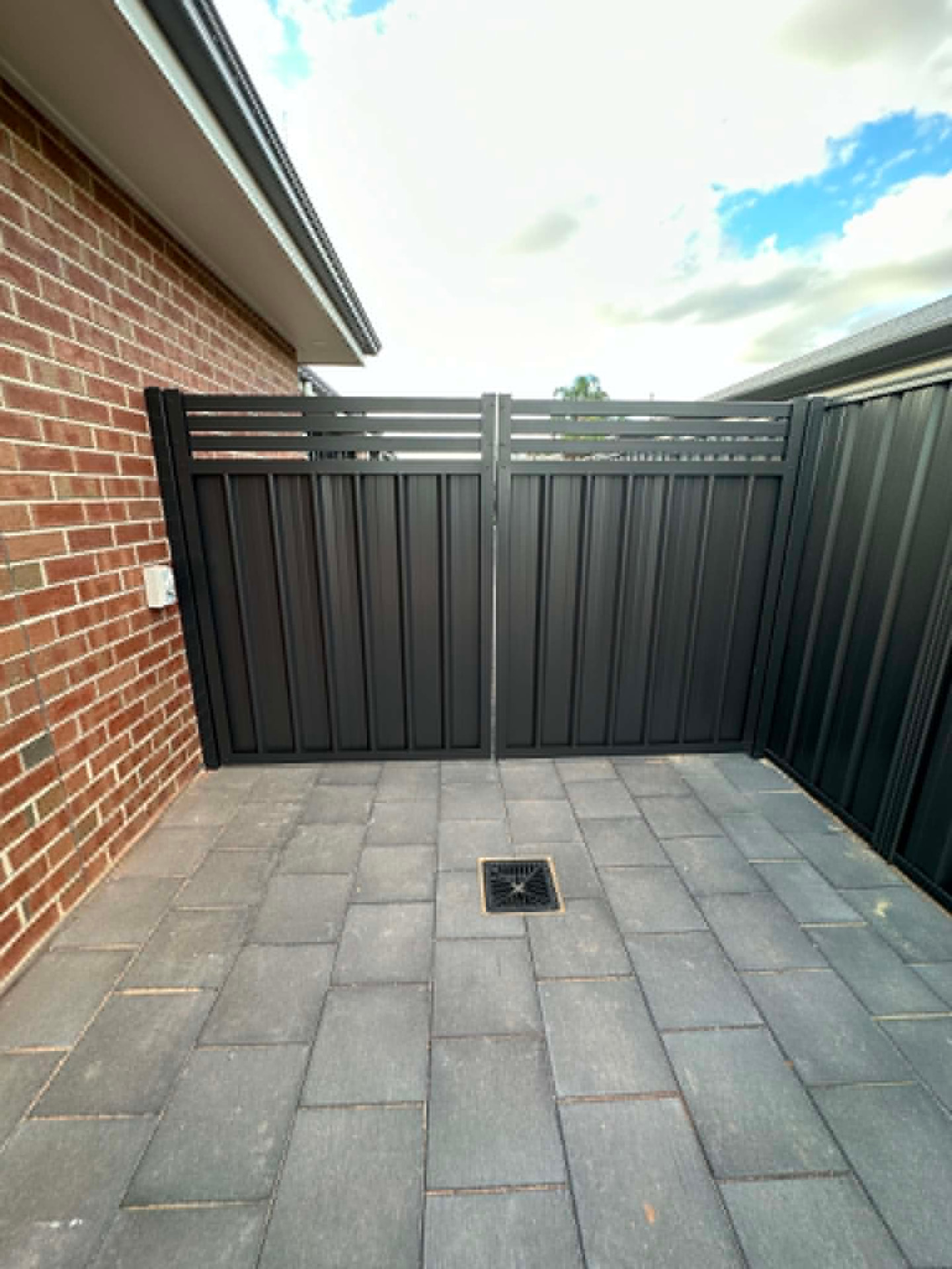 Custom double swing gates viewed straight-on from the paved area, showing the vertical steel infill and horizontal slat top detail