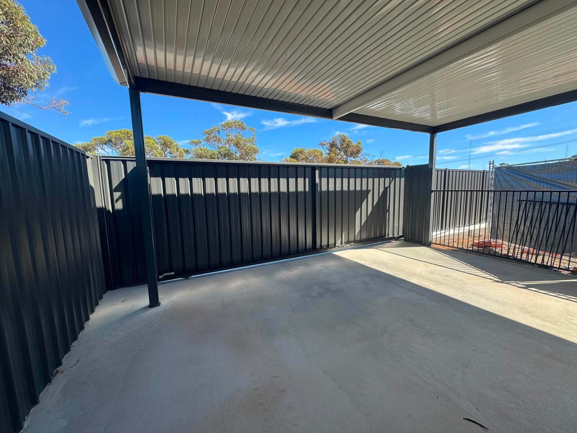 Charcoal Good Neighbour colorbond fencing with a sliding gate beside a covered concrete area