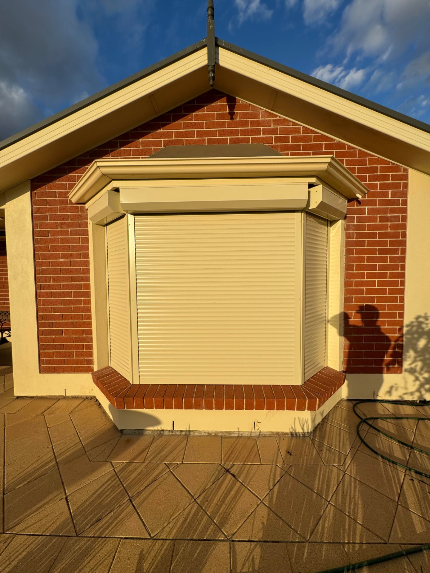 Cream roller shutters closed over a residential brick bay window