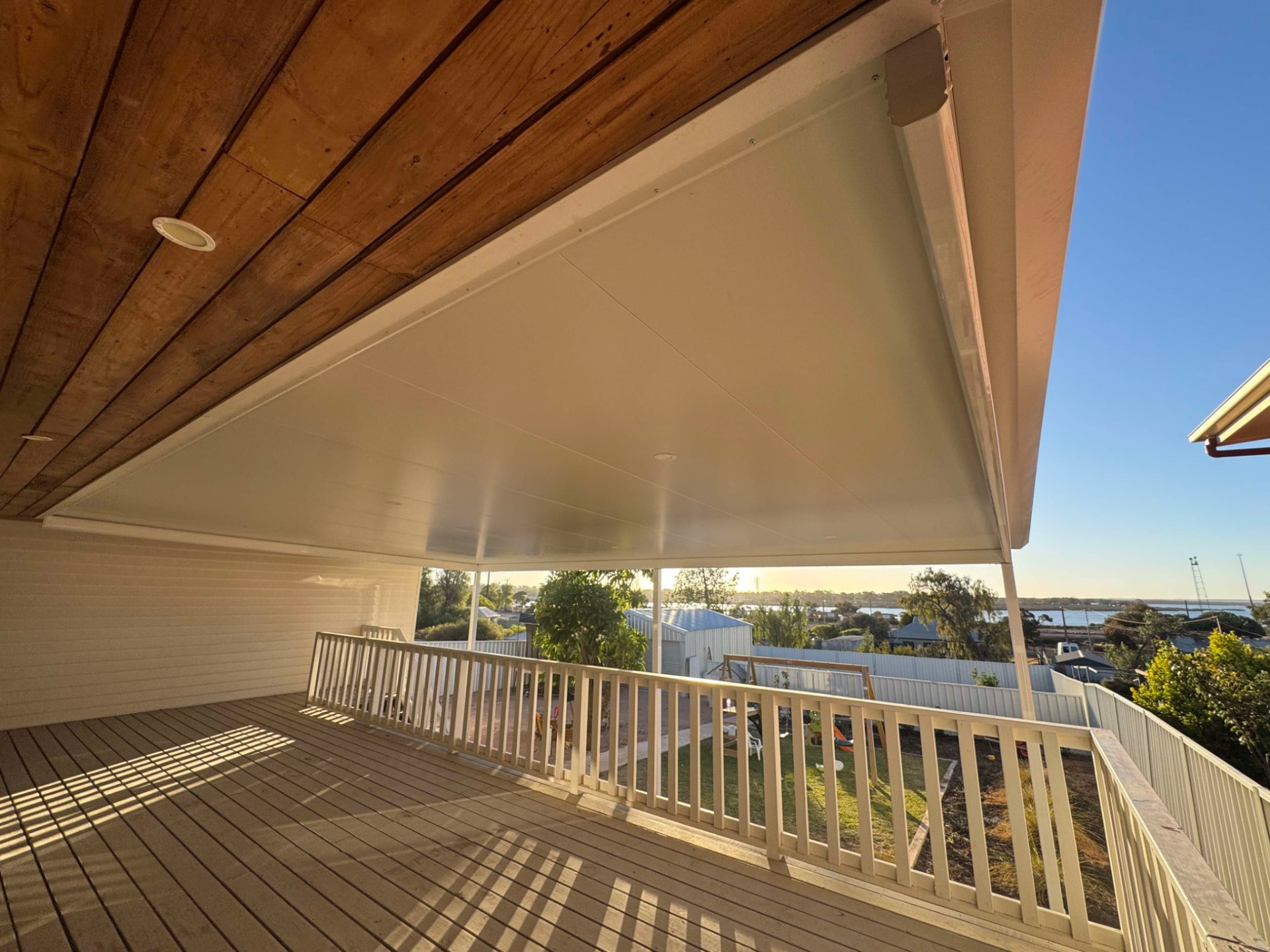Stratco attached verandah with 75mm Cooldek insulated ceiling over an elevated timber deck, white balustrade and integrated downlights