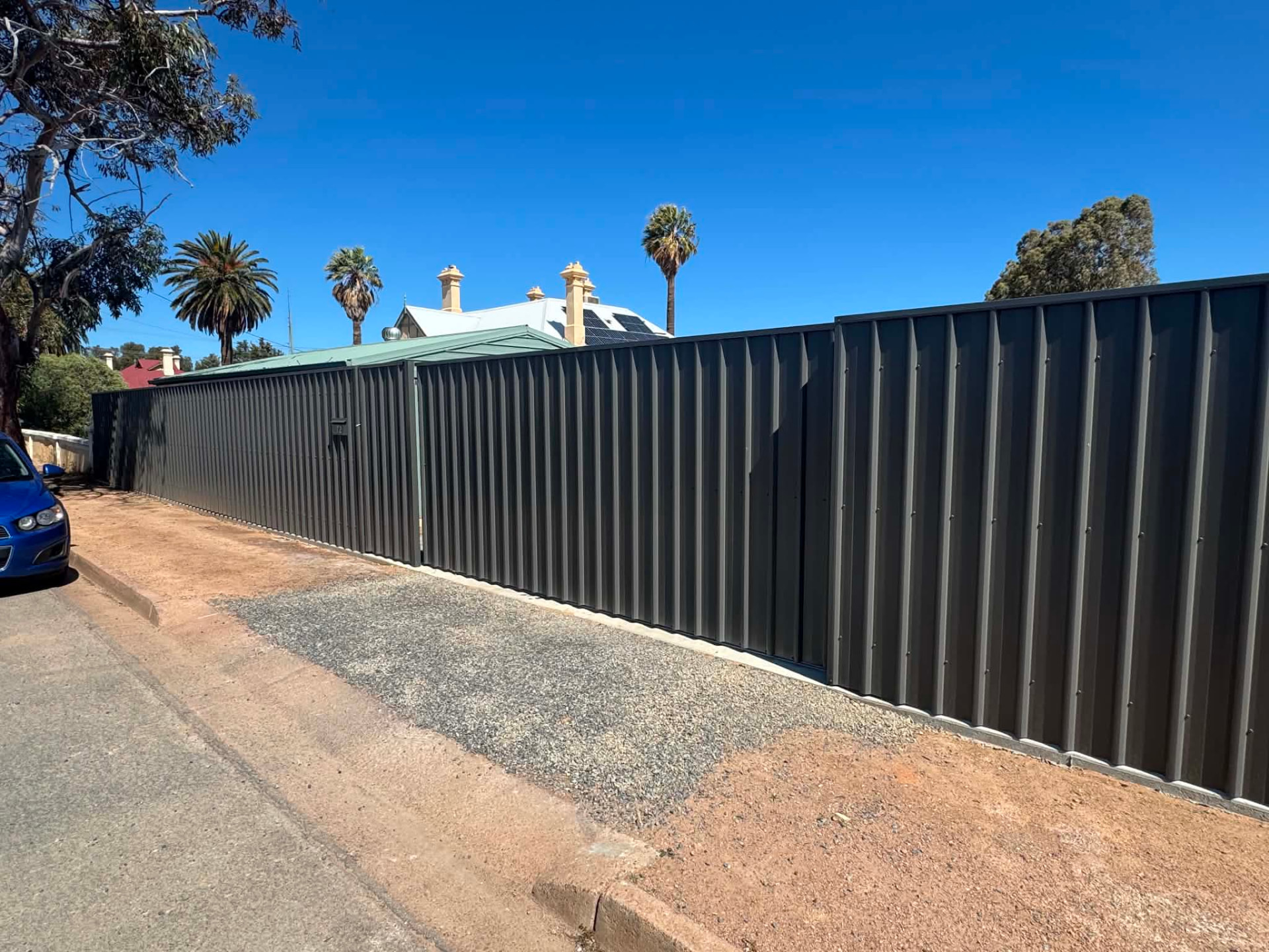 Long dark boundary fence line with matching gates along a street frontage